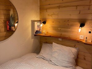 Ein gemütliches Schlafzimmer mit einem Holzkopfteil, einem runden Spiegel und zwei Wandleuchten zum Lesen.
