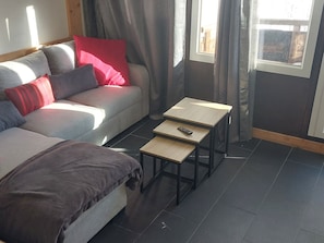 Uma sala de estar moderna com um sofá, duas mesinhas e uma janela com cortinas.