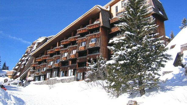 Un hotel de varios pisos con balcones, rodeado de árboles nevados y un cielo azul claro.
