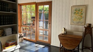 A room with a wooden floor, a bookshelf, a dining table, and a large window with a view of greenery.