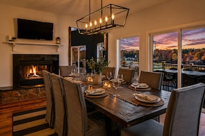 A dining room with a fireplace, a large window with a scenic view, and a modern chandelier.