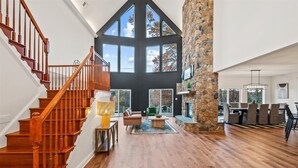 Un salón amplio con escalera de madera, ventanas grandes y una pared de acento de piedra.