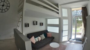 Un salon moderne avec un canapé foncé, une table basse ronde et une grande fenêtre donnant sur l’extérieur.