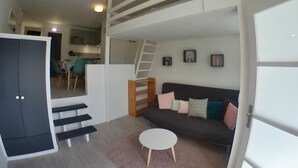 Un espace de vie compact comprenant un escalier menant à un niveau supérieur, un canapé avec des coussins, une petite table ronde et une armoire.