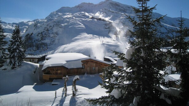 Une montagne enneigée, avec un chalet en bois au premier plan.