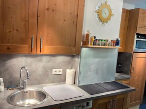 Une cuisine avec des armoires en bois, un évier en acier inoxydable, une cuisinière encastrée et une étagère contenant divers objets.