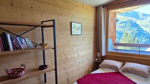 Ein Zimmer mit Holzwänden, einem Bett, einem Bücherregal und einem Fenster mit Blick auf die Berge.