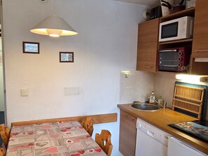 Uma cozinha compacta com micro-ondas, torradeira e lava-louças. Há uma mesa de jantar com cadeiras e um lustre.