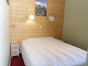Une chambre avec un mur en bois, un lit avec une literie blanche, deux lampes de chevet et une petite table de chevet avec des tiroirs.