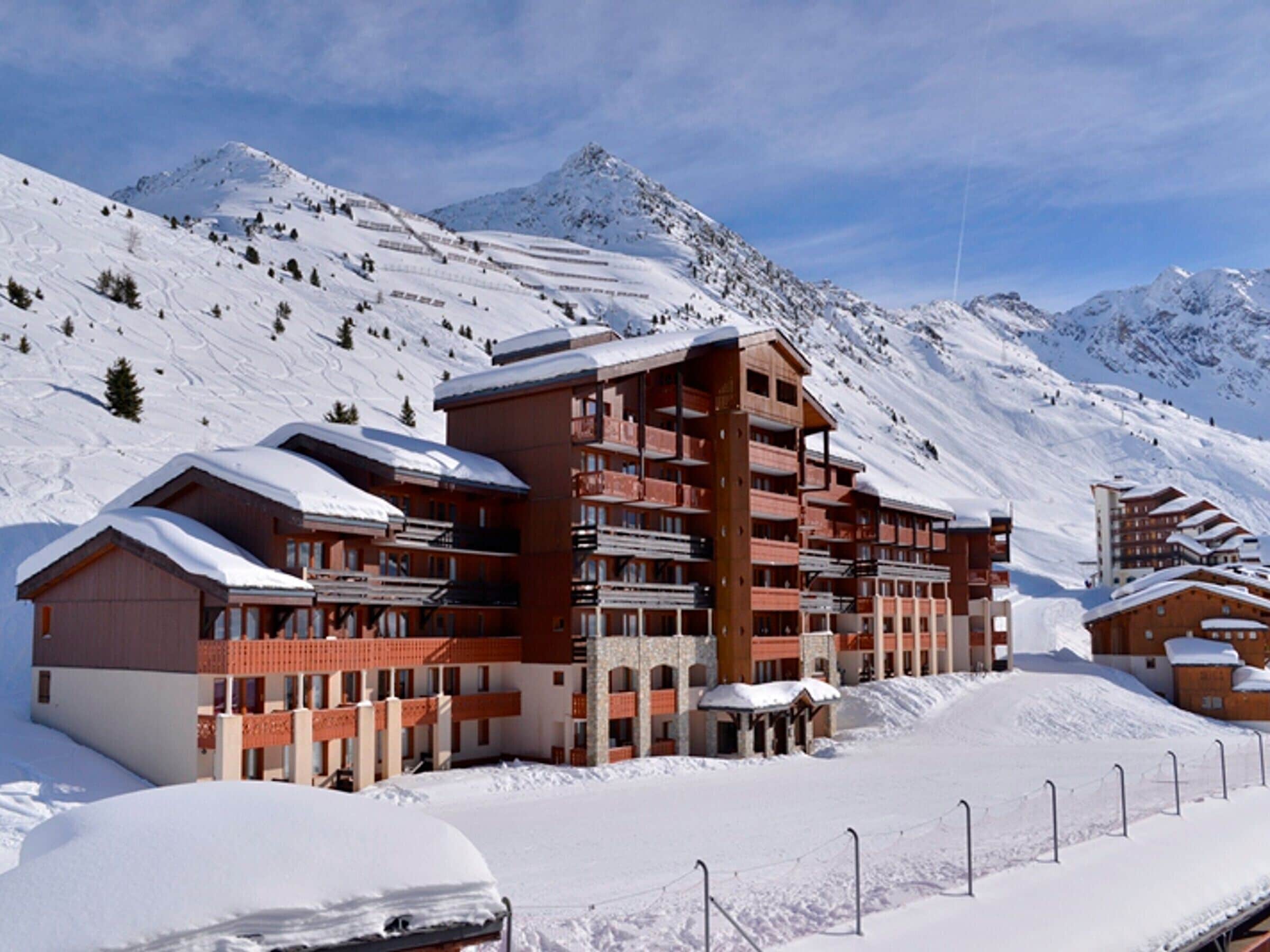 Un hôtel à plusieurs étages, doté de balcons, qui se dresse sur fond de montagnes enneigées.