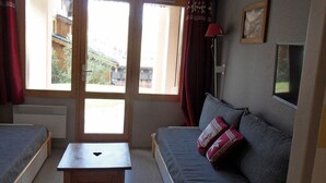 Una habitación con dos camas, una mesita, un sofá con cojines, una lámpara y una ventana con cortinas.
