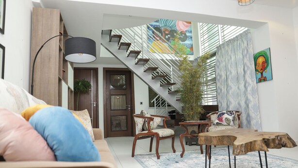 A modern living room with a staircase, wooden furniture, and a large window. - Cozy bohemian loft in the heart of Lekki. Close to the beach, art gallery & mall (Lekki)