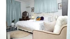 A bedroom with a bed, a chair, a bedside table, a lamp, a mirror, and curtains. - Cozy bohemian loft in the heart of Lekki. Close to the beach, art gallery & mall (Lekki)