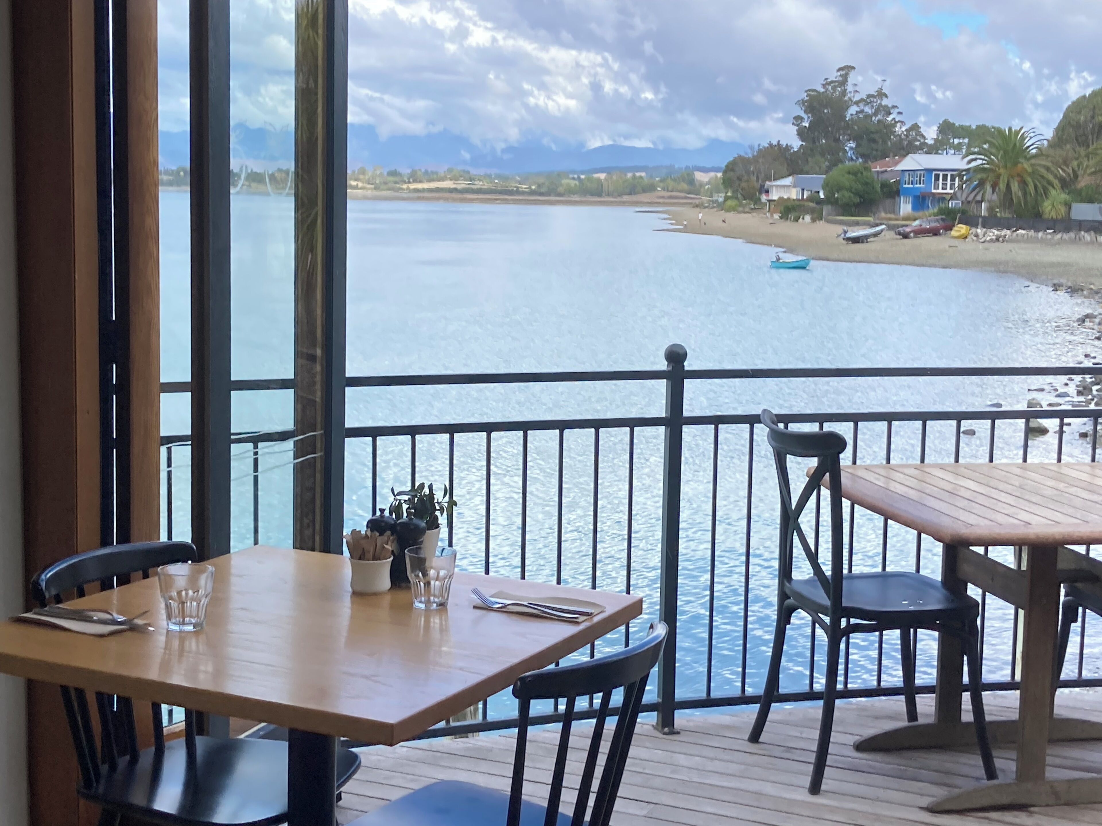 A dining area with a view of a calm body of water, a wooden deck, and a railing.