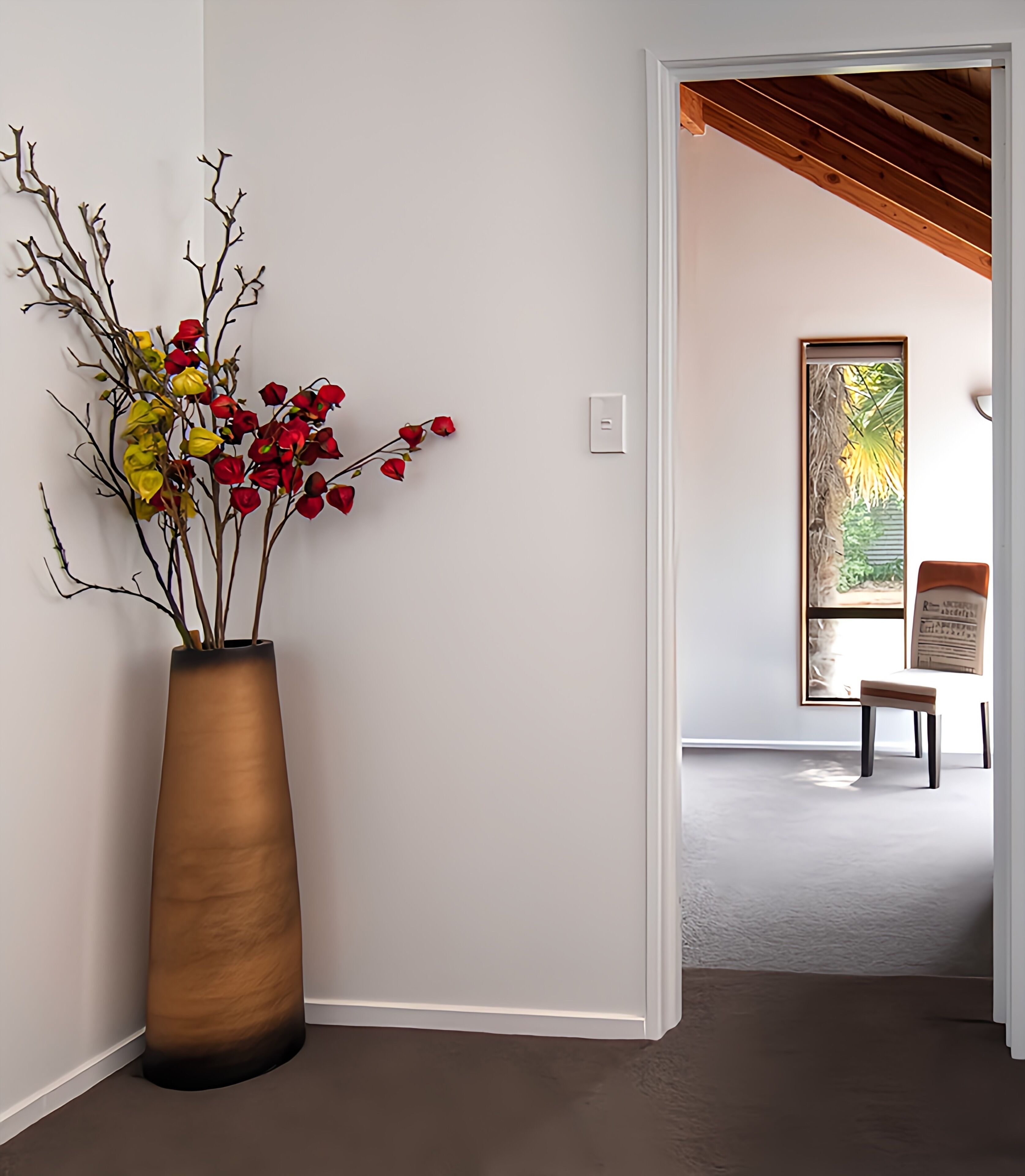 A hallway with a large vase of flowers, a wooden bench, and a view of a garden through a window.