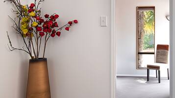 A hallway with a large vase of flowers, a wooden bench, and a view of a garden through a window.