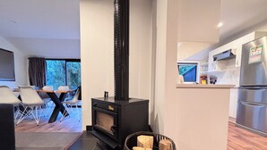 A modern living room with a black wood-burning stove, a dining area with chairs, and a kitchen with stainless steel appliances. - 6 Bedroom Family Gateway in the Heart of Mapua Village (Māpua)