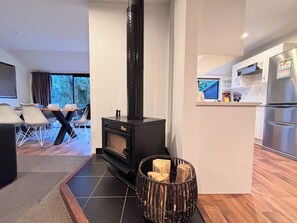 A modern living room with a black wood-burning stove, a dining area with chairs, and a kitchen with stainless steel appliances. - 6 Bedroom Family Gateway in the Heart of Mapua Village (Māpua)