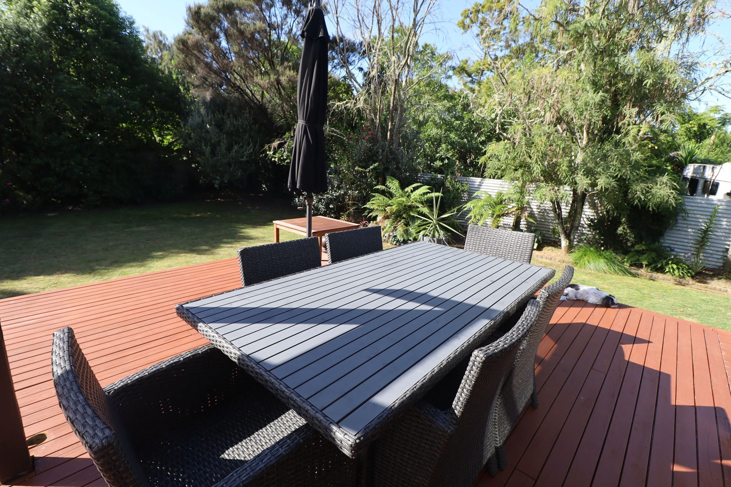 Une terrasse avec une table et des chaises, entourée de verdure et d’arbres.