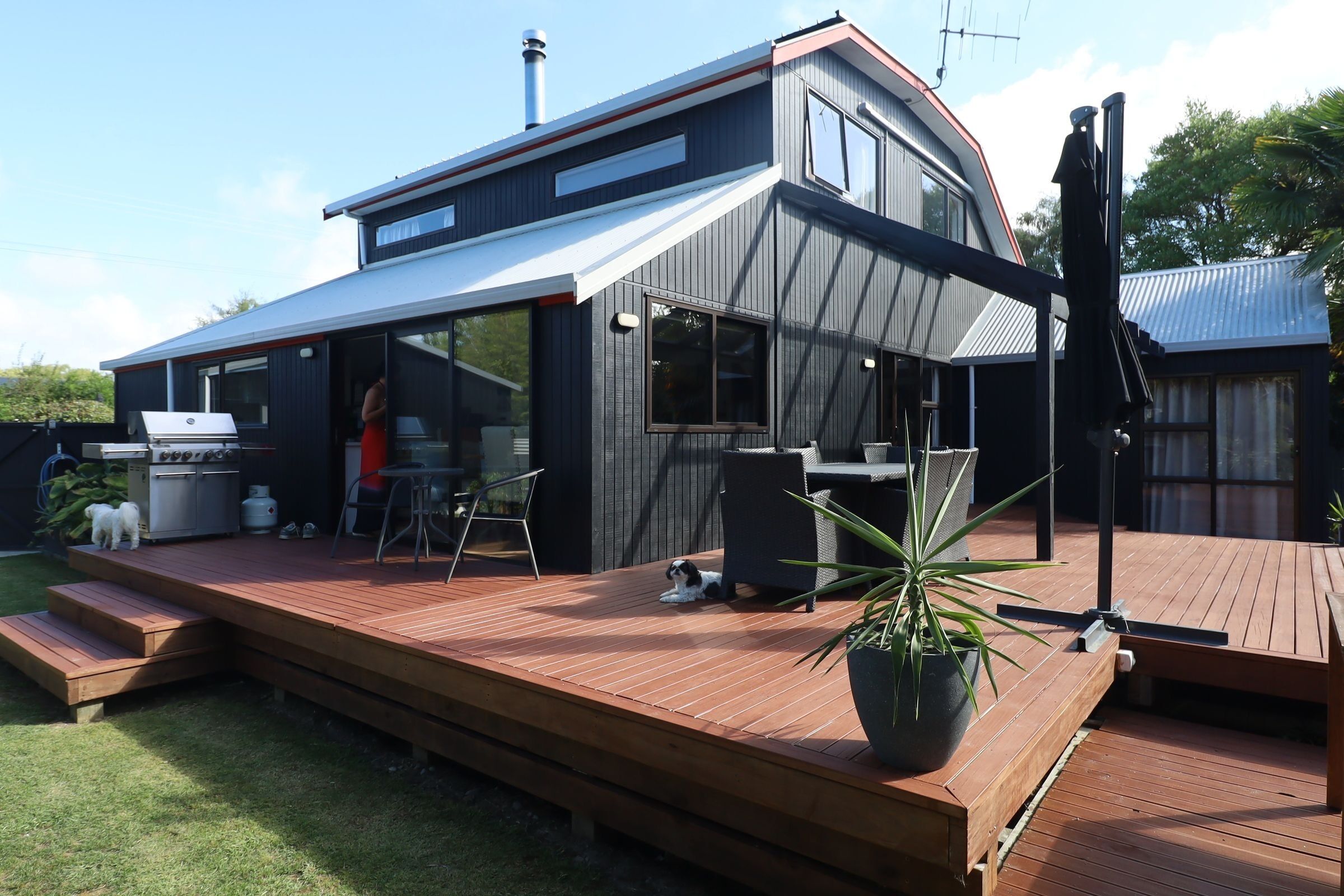 Una casa moderna de dos pisos con un deck, una zona de barbacoa y un gran ventanal con vista al jardín.