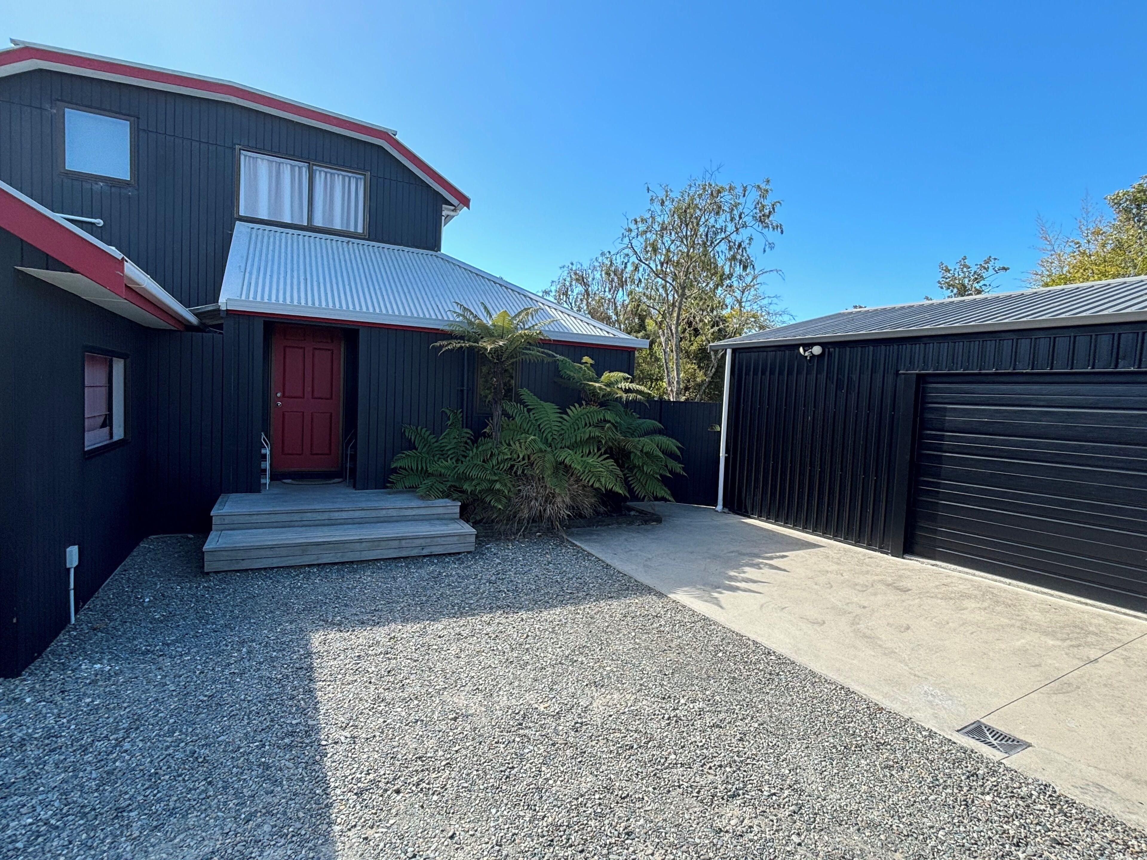 Un bâtiment à deux étages avec une porte rouge, un garage et une allée gravillonnée.