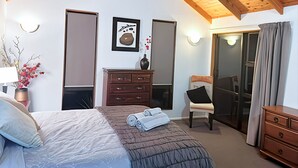 A bedroom with a bed, dresser, chair, and a sliding glass door. - 6 Bedroom Family Gateway in the Heart of Mapua Village (Māpua)