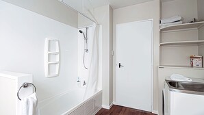 A bathroom with a bathtub, shower, and a white door. - 6 Bedroom Family Gateway in the Heart of Mapua Village (Māpua)