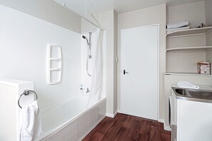 A bathroom with a bathtub, shower, and a white door. - 6 Bedroom Family Gateway in the Heart of Mapua Village (Māpua)