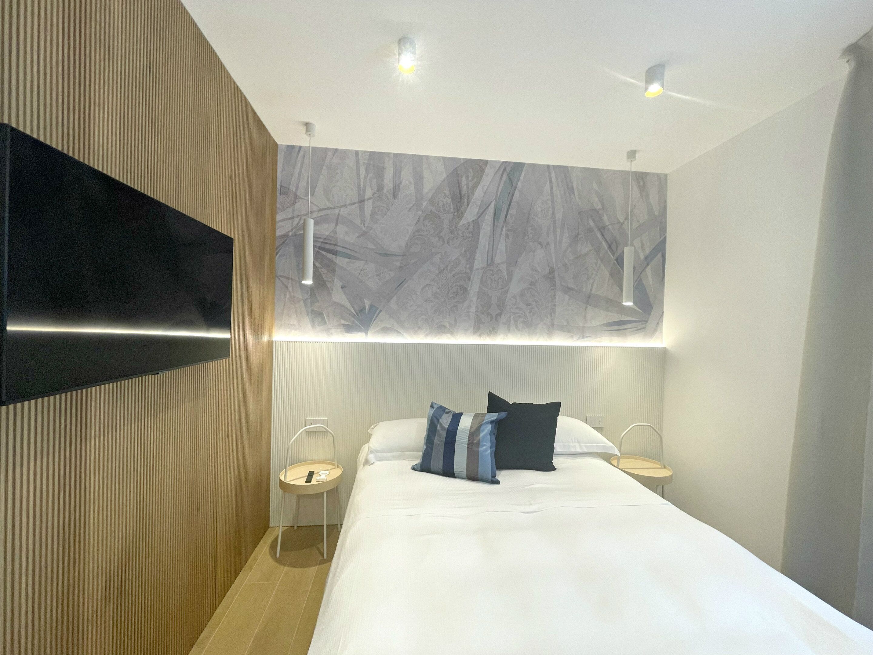 Une chambre d’hôtel moderne dotée d’un grand lit, d’un téléviseur à écran plat fixé au mur et d’une fresque murale abstraite originale au-dessus du lit.
