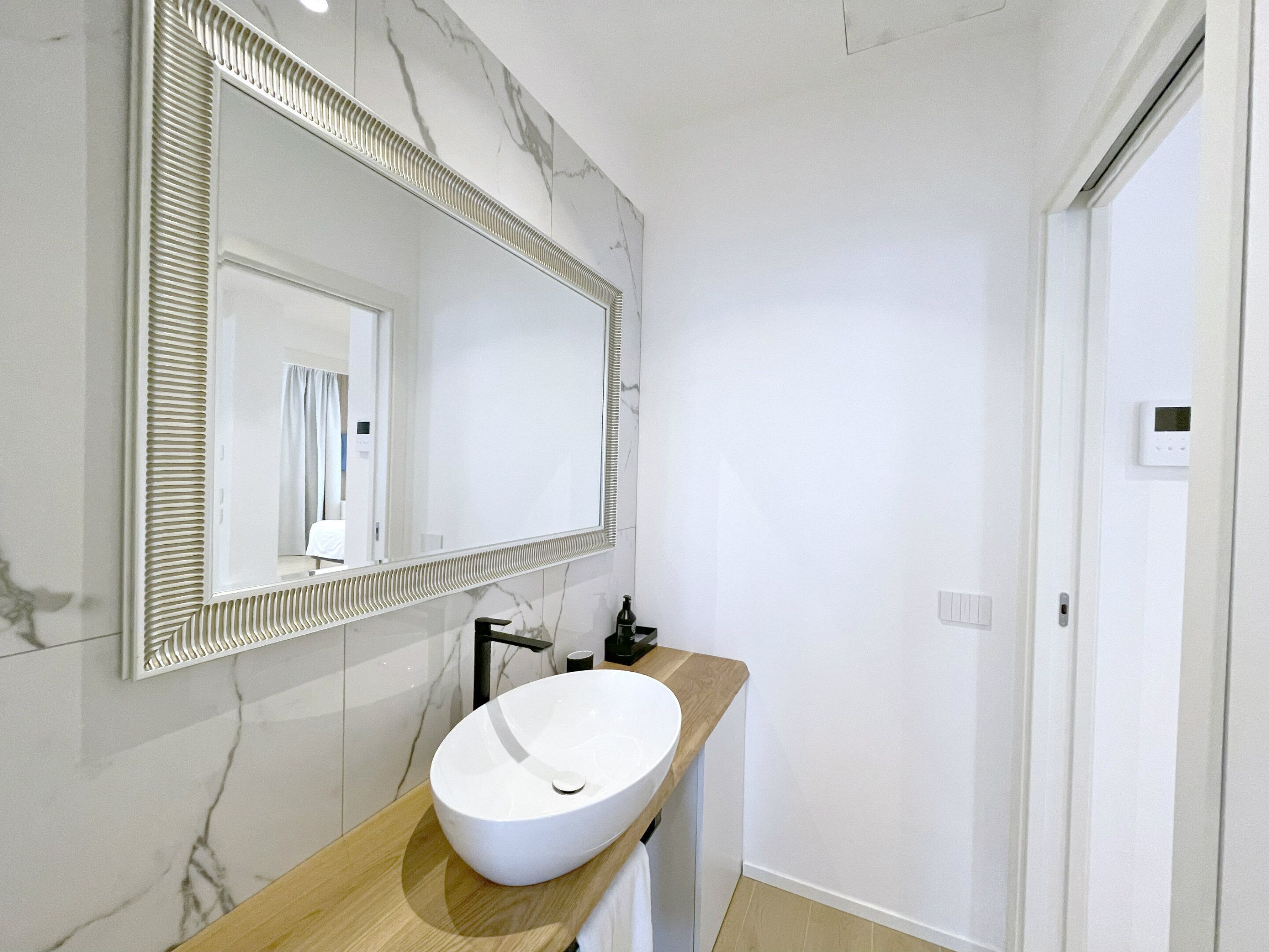 Un bagno moderno con uno specchio grande, un lavabo sospeso bianco e un piano d'appoggio in legno.