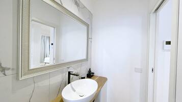 Un bagno moderno con uno specchio grande, un lavabo sospeso bianco e un piano d'appoggio in legno.