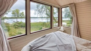 A bedroom with a bed, a nightstand, and a view of a lake through large windows. - Awesome home in älmhult with lake view (Älmhult)