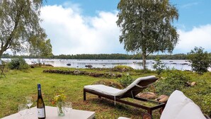 A lakeside outdoor seating area with a table, chairs, and a bottle of wine. - Awesome home in älmhult with lake view (Älmhult)