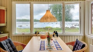 A dining area with a table set for two, overlooking a lake with rocks and trees. - Awesome home in älmhult with lake view (Älmhult)