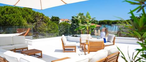 A rooftop terrace with white cushioned seating, wooden tables, and a large umbrella.