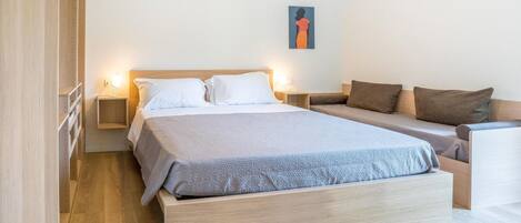A modern bedroom with a large bed, a sofa, and a nightstand with a lamp.