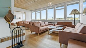 Amplia sala de estar con sofás de cuero, piso de madera, ventanas grandes y un techo con listones de madera.
