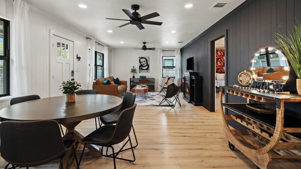 Una sala de estar moderna con comedor, chimenea, ventiladores de techo y un carrito de bar.