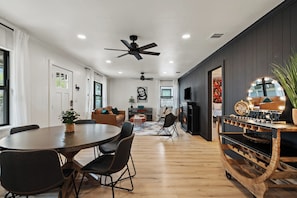 A modern living room with a round dining table, dark wood flooring, ceiling fans, and a fireplace. - Das Green Dor - Sleeps 9, Hot Tub & Fire Pit (Fredericksburg)
