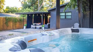 Un jacuzzi con etiqueta de advertencia, un área de estar techada y una casa al fondo.