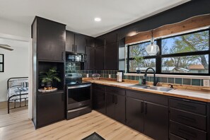 A modern kitchen with dark cabinetry, a wooden countertop, and a large window.