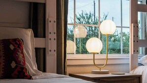 Et hotelværelse med en seng, et natbord med en lampe og et vindue med dekorativ belysning.