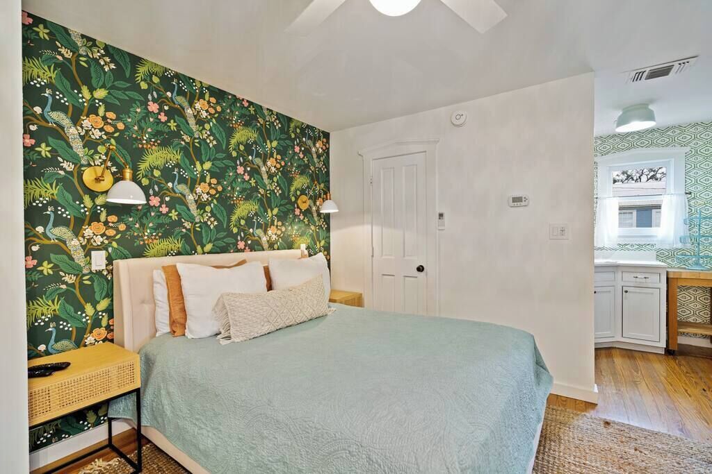 A bedroom with a bed, a nightstand, a lamp, a door, and a view of a bathroom.
