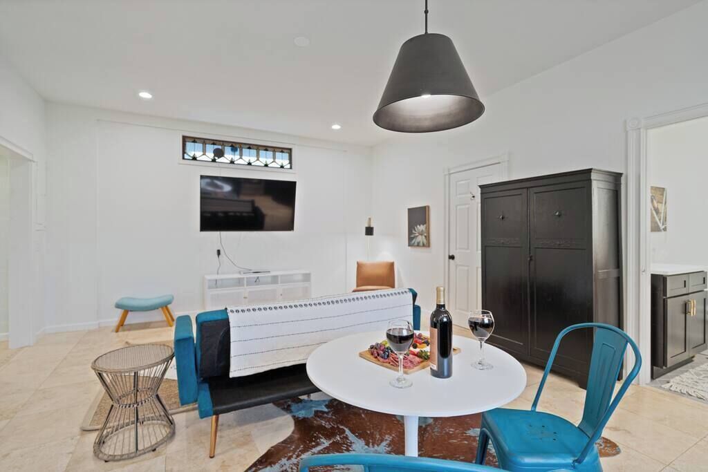 Una sala moderna con sofá, una mesa redonda con vino y un televisor en la pared.