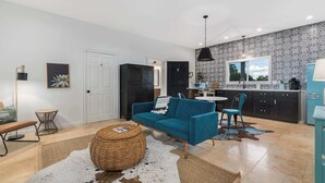 A modern living room with a blue sofa, a round coffee table, and a kitchen area with a patterned backsplash. - Stonewall Bungalow 3 - Sleeps 4 (Stonewall)