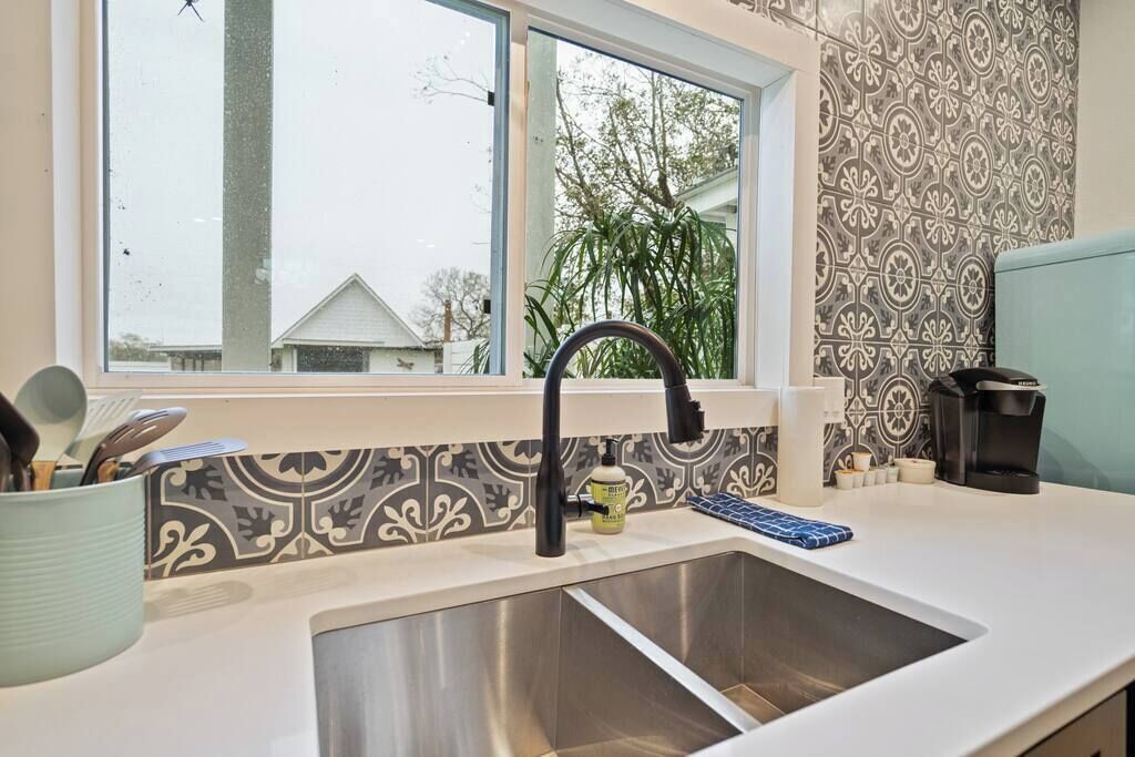 A kitchen with a stainless steel sink, a window, and patterned backsplash.