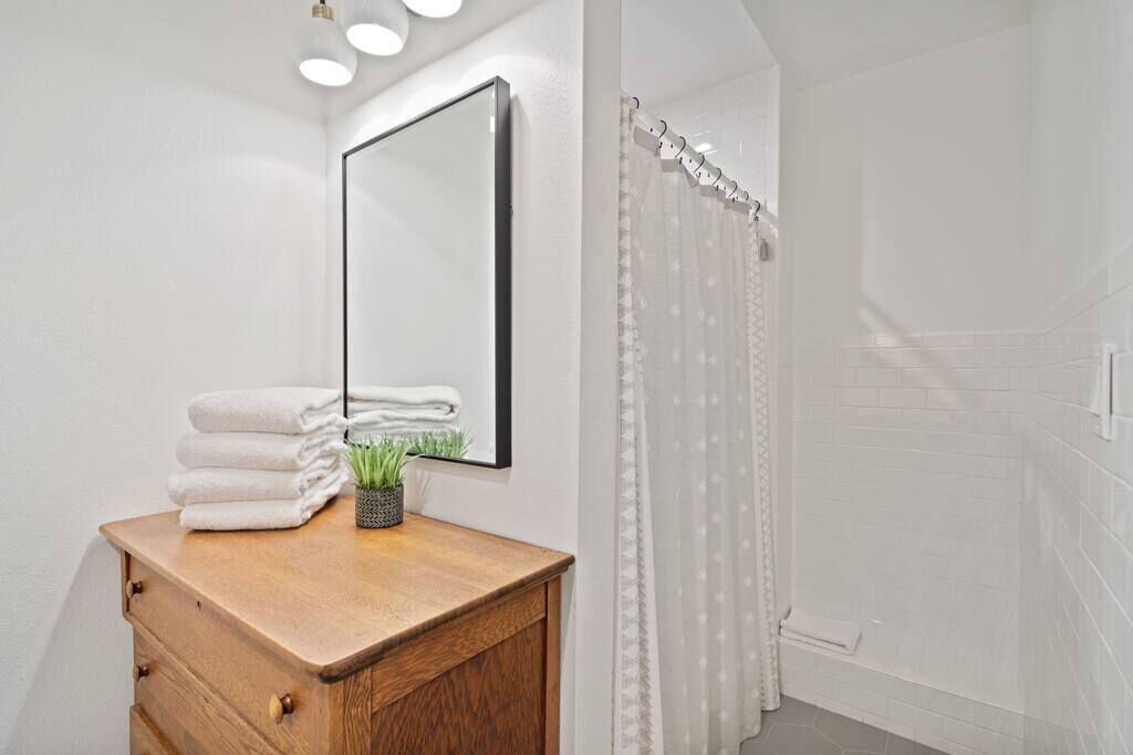 A bathroom with a wooden vanity, a mirror, a stack of towels, and a shower curtain.