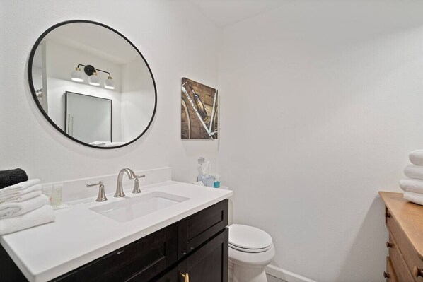 Un baño con un lavabo blanco, un espejo, un inodoro y un mueble de madera con toallas.