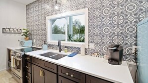 A kitchen with a patterned backsplash, a window, a coffee maker, and a vintage radio. - Stonewall Bungalow 3 - Sleeps 4 (Stonewall)