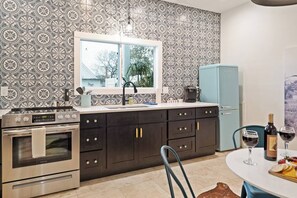 Una cucina con carta da parati decorata, una finestra, un fornello, un frigorifero e un tavolo da pranzo con bicchieri da vino.